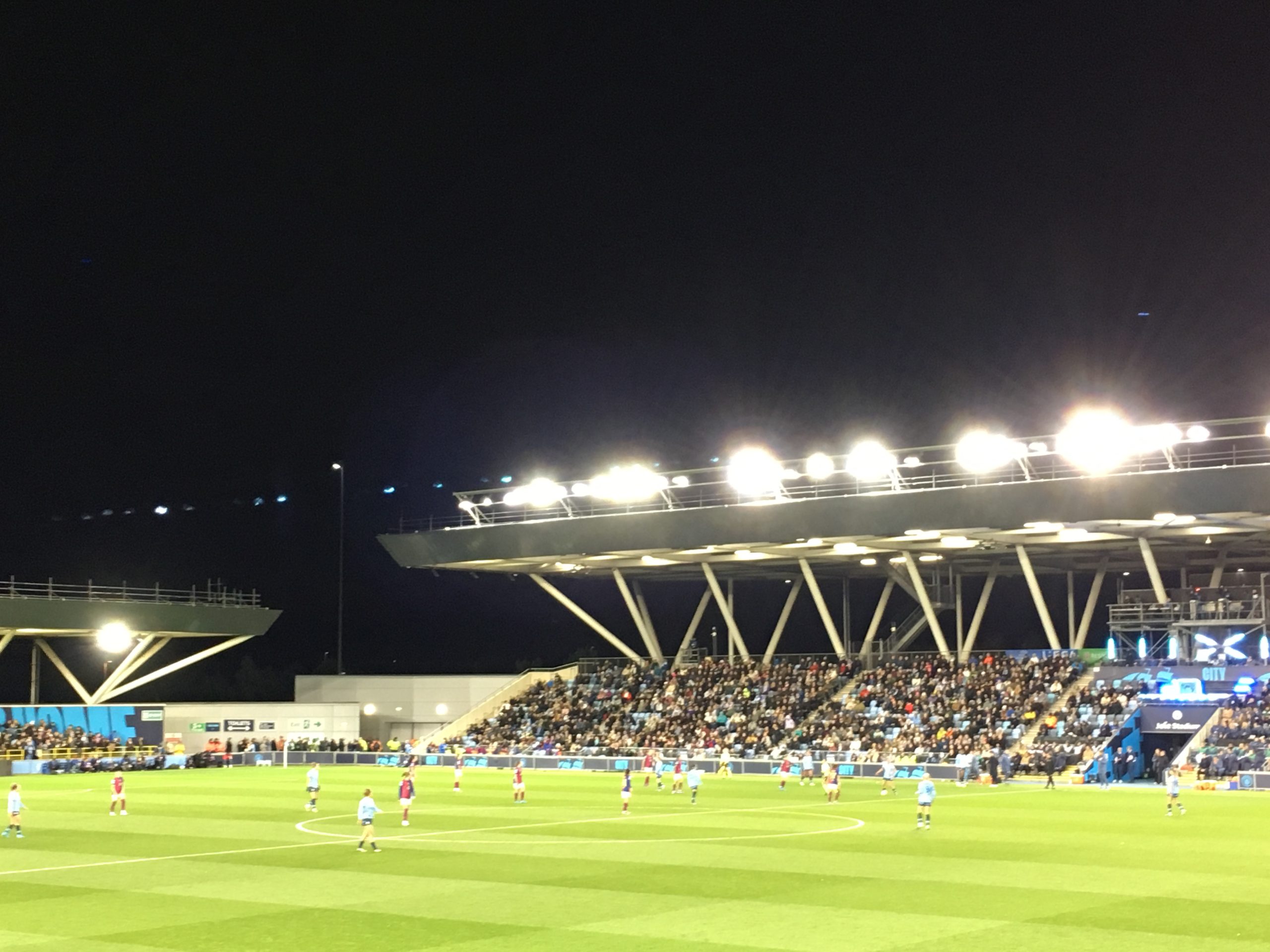 The Joie Stadium at night, floodlight illuminating Barça Femení and Man City players